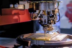 半導体パッケージング工程で使用されるワイヤボンダー装置のクローズアップ。精密なボンディングヘッドのキャピラリがリードフレーム上のチップに向かってワイヤを供給している